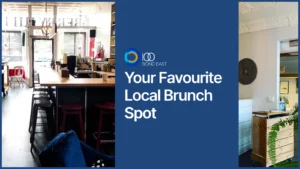 Cozy café interior with wooden bar counter, stools, coffee equipment, and bright front windows, with a hallway and host stand visible on the right side
